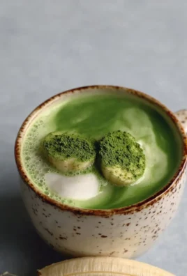 Creamy banana cream matcha latte in a glass garnished with banana slices.