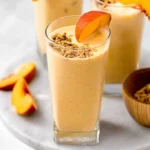Banana Peach Protein Smoothie in a glass with fruits on the side