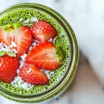 A vibrant bowl of Strawberry Matcha Overnight oats topped with fresh strawberries.