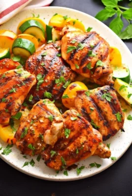 Lemon-herb grilled chicken thighs garnished with herbs on a grill plate.