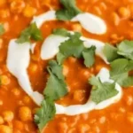 Bowl of vegan chickpea curry with spices and herbs, served with rice.