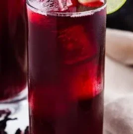 A glass of homemade hibiscus water with vibrant red color on a wooden table.