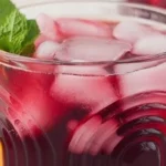 Glass of refreshing iced hibiscus tea with flowers and ice cubes
