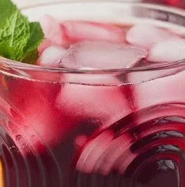 Glass of refreshing iced hibiscus tea with flowers and ice cubes