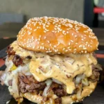 Delicious smash burgers topped with baconnaise sauce on a wooden plate.
